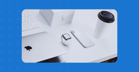 Apple products on a table including an iPhone, Mac Book, and Apple Watch.